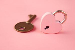 cadeado em formato de coração rosa e chave na mesa foto