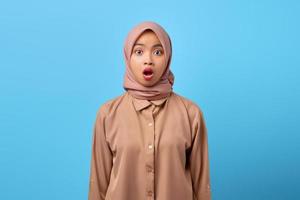 retrato de uma jovem asiática chocada com a boca aberta usando um hijab sobre fundo azul