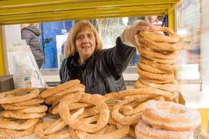 Atenas, Grécia, dezembro 23, 2023 mulher rua fornecedor vendendo a saboroso Koulouri ou pão argolas uma tradicional grego rua Comida encontrado através Atenas foto