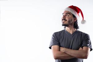 retrato de homem latino sorridente com chapéu de Natal, olhando para o lado com os braços cruzados. fundo branco foto