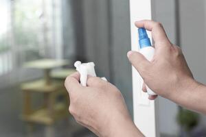 uma homem pressione álcool garrafa spray para limpeza porta lidar com e usar branco fiapo limpeza e primário doença prevenção dentro casa foto