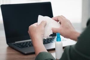 fechar acima mão uma homem limpeza e desinfecção do área de trabalho. desinfecção lenços para limpar superfície do escrivaninha , computador portátil, rato às escritório. Pare a espalhar foto