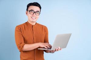 jovem empresário asiático usando laptop sobre fundo azul foto
