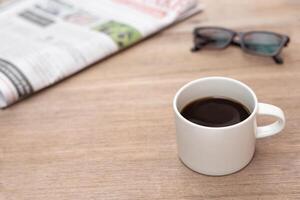 café copo óculos e jornal em madeira mesa lendo notícia dentro a tradicional mundo não social rede foto