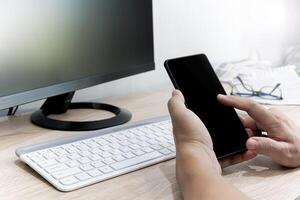uma homem usar inteligente telefone procurar uma notícia e blog dados em a Internet com computador portátil e notícia papel em a madeira mesa foto