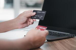 uma homem aguarde crédito cartão dentro seu mão e olhando número com computador portátil computador em madeira mesa para compras conectados ordem casa compras e Entrega conceito foto