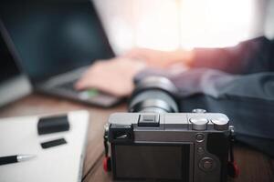 fechar acima Câmera com uma homem usar computador portátil trabalhando e fotografia equipamento em mesa foto