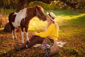 mulher e visto Castanho pónei às pôr do sol dentro floresta, lindo menina dentro outono roupas O amor é dela cavalo, conceito do gentileza, animal Cuidado, natureza e amizade. flores foto