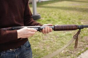 uma homem cobranças uma ação de bomba espingarda com uma munição. 12 calibre. pneu ar livre. uma homem dentro fones de ouvido e óculos é preparando para atirar. armas de fogo para Esportes tiroteio, passatempo. foto