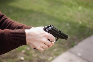 uma homem cobranças uma arma de fogo contra uma verde grama. armas de fogo arma de fogo ar livre. esporte, hobbies cópia de espaço foto