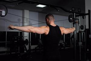 retrato do a atleta, uma Esportes homem treinador faz a exercício em simulador dentro a academia. saudável ativo estilo de vida, shakes músculos. traseiro Visão foto