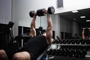 homem executa a exercício com halteres em uma simulador dentro a academia. atleta, fisiculturista, ginástica treinador. muscular sexy corpo. foto