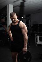 retrato do uma bonito homem dentro academia. treinador, atleta, fisiculturista, muscular sexy corpo, escuridão. foto