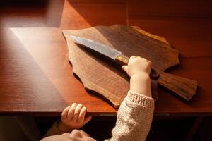 a criança puxa uma faca a partir de a mesa. a criança pode corte, crianças casa perigos. uma pequeno um ano de idade menina com uma faca. foto