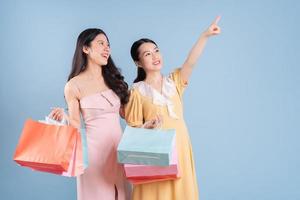 duas jovens mulheres asiáticas segurando uma sacola de compras sobre fundo azul foto