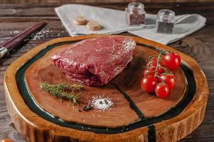 Picanha crua - picanha brasileira em uma tábua de madeira com ramo de alecrim, tomate e especiarias. foto