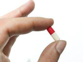 dedos do uma mão segurando uma cápsula comprimido isolado em uma branco fundo foto