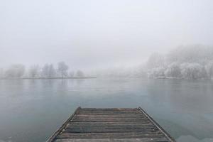 paisagem de inverno à noite. cais de madeira ao longo de um belo lago congelado. árvores com geada, cenário de inverno sazonal calmo. vista pacífica e branca foto