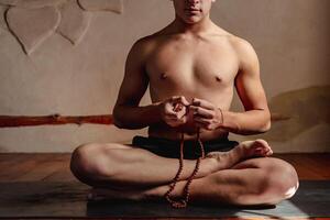 jovem irreconhecível homem meditando com uma rudraksha mala dentro dele mãos. foto