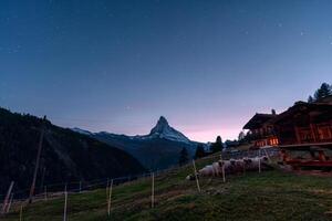 noite cena do matterhorn montanha com estrelado e rebanho do ovelha dentro impedir de de madeira cabana às zermatt, Suíça foto