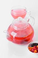 delicioso chá de bagas e frutas em um lindo bule de vidro em um fundo branco com reflexo foto