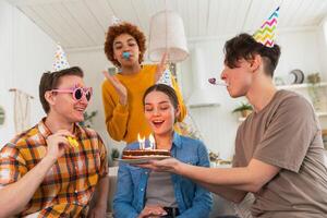 faço uma desejar. mulher vestindo festa boné sopro Fora queimando velas em aniversário bolo. feliz aniversário Festa. grupo do amigos desejos menina feliz aniversário. pessoas a comemorar aniversário com festa às casa foto