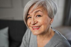 retrato do confiante à moda europeu meio envelhecido Senior mulher. Mais velho maduro anos 60 senhora sorridente às lar. feliz atraente Senior fêmea olhando Câmera fechar acima face Tiros na Cabeça retrato. feliz pessoas foto