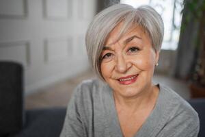 retrato do confiante à moda europeu meio envelhecido Senior mulher. Mais velho maduro anos 60 senhora sorridente às lar. feliz atraente Senior fêmea olhando Câmera fechar acima face Tiros na Cabeça retrato. feliz pessoas foto