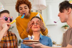 faço uma desejar. mulher vestindo festa boné sopro Fora queimando velas em aniversário bolo. feliz aniversário Festa. grupo do amigos desejos menina feliz aniversário. pessoas a comemorar aniversário com festa às casa foto