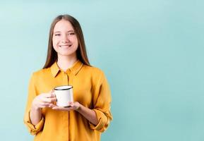 jovem mulher caucasiana usando um copo de café ou chá sobre fundo azul