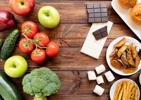 conceito de comida saudável e não saudável. frutas e verduras vs doces e batata frita vista de cima plana sobre fundo de madeira foto