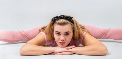 linda mulher vestindo roupas esportivas rosa, alongando-se em uma pose de perna dividida no estúdio isolado em um fundo cinza foto