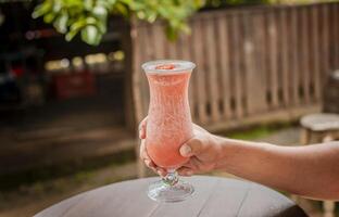 mãos mostrando morango batido em de madeira mesa. pessoas mão segurando uma morango milkshake em madeira, mãos segurando morango batido em de madeira mesa com borrado fundo foto