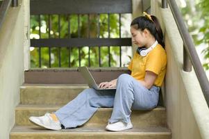 adolescente sentada na escada com um laptop trabalhando em casa. foto