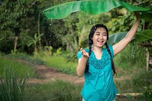 retrato de uma jovem asiática com cabelo preto segurando uma folha de bananeira na chuva no fundo do jardim verde foto