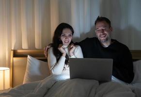 casal cuacasiano assistindo filmes de terror durante o programa no computador juntos na cama em casa à noite