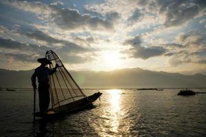 silhueta de pescador local usando galinheiro para pegar no lago inle ao amanhecer foto