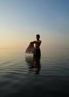 no lago, jovem asiático usando armadilha de bambu para pescar de manhã foto