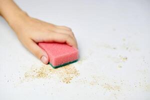 limpeza da mesa da cozinha. esponja rosa na mão da mulher remove sujeira, migalhas de pão e sobras. tarefas domésticas foto