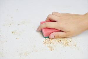 limpeza da mesa da cozinha. esponja rosa na mão da mulher remove sujeira, migalhas de pão e sobras. tarefas domésticas foto