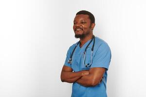 sorridente Preto cirurgião médico barbudo homem cruzado braços dentro azul casaco com estetoscópio branco fundo foto