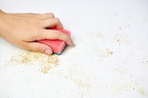 esponja na mão da mulher remove sujeira, migalhas de pão e sobras. limpeza da mesa da cozinha. tarefas domésticas foto