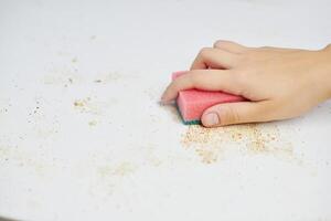 limpeza da mesa da cozinha. esponja rosa na mão da mulher remove sujeira, migalhas de pão e sobras. tarefas domésticas foto