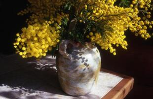 uma vaso preenchidas com amarelo flores sentado em uma mesa foto