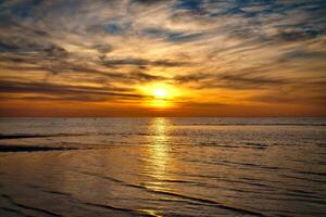 pôr do sol, iluminado mar. arenoso de praia dentro a primeiro plano. luz ondas. báltico mar foto