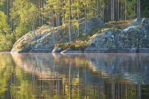 em uma lago dentro Suécia dentro pequeno e. Rocha dentro primeiro plano, azul água, ensolarado céu, foto