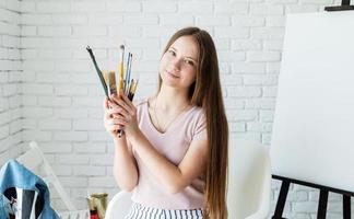 mulher sorridente artista segurando pincéis trabalhando em seu estúdio foto