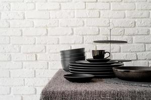 pilha de pratos e talheres de cerâmica preta na mesa no fundo da parede de tijolo branco