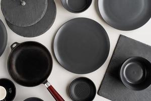 pilhas de pratos de cerâmica preta e vista superior de talheres em fundo cinza