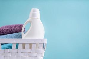 cesto de roupa suja com um frasco de detergente e uma pilha de toalhas limpas na mesa branca isolada sobre fundo azul foto